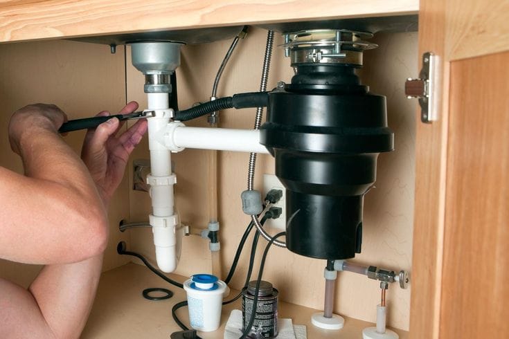 Plumber installing a garbage disposal beneath a kitchen sink in Bradenton