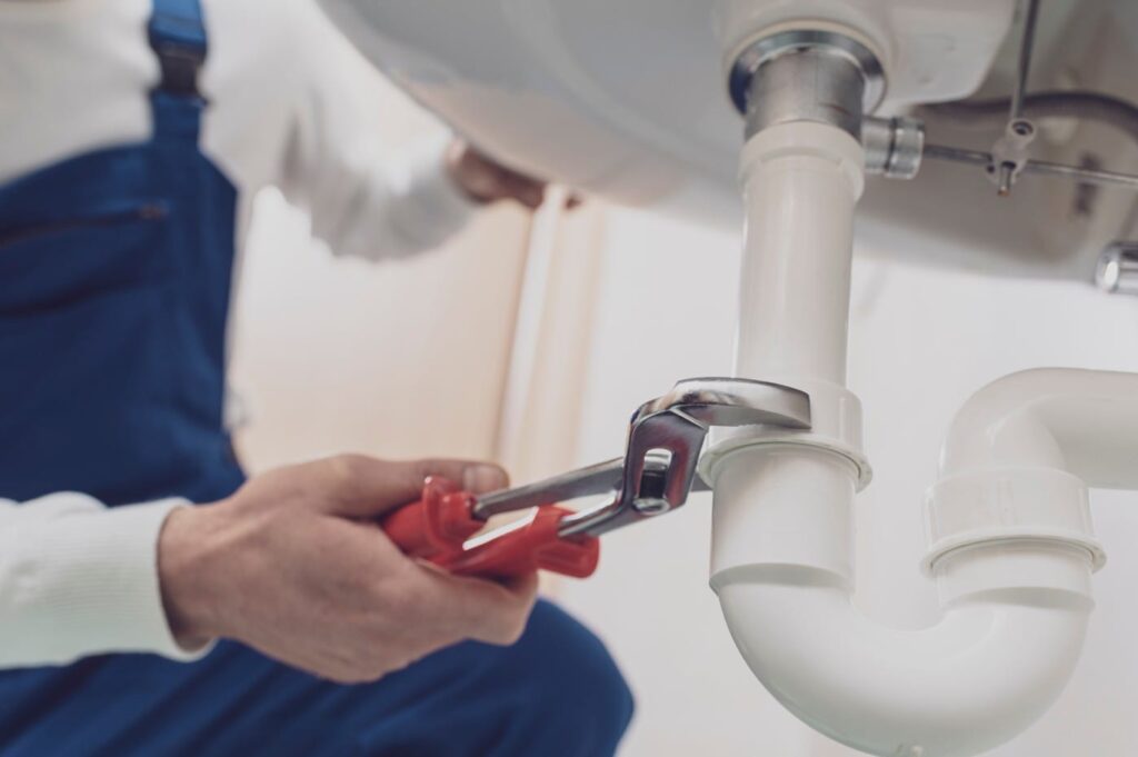 Plumber repairing a white drain pipe beneath a sink in Bradenton